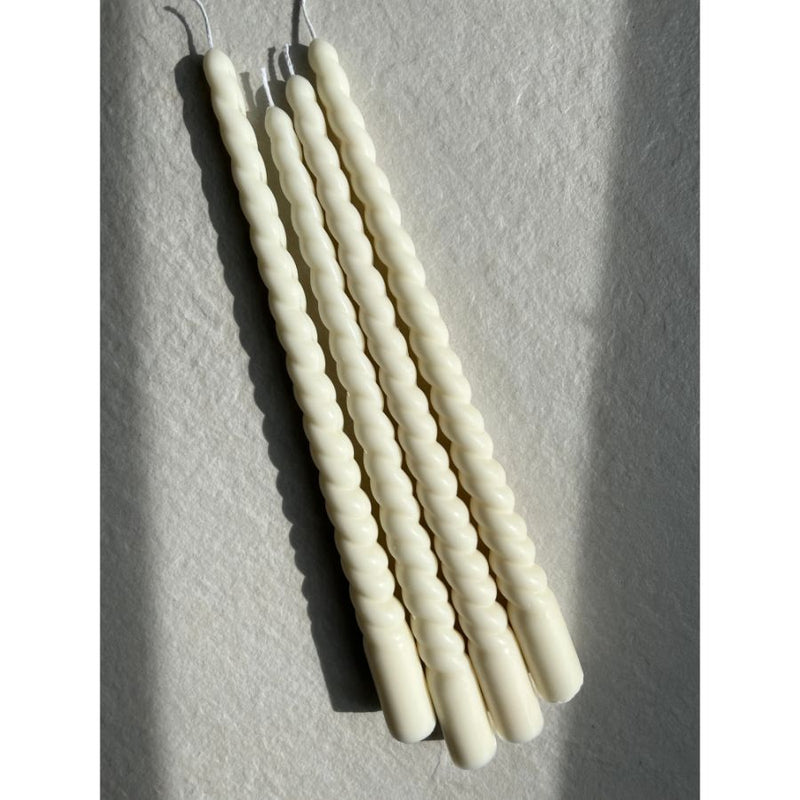 Four white ribbed spiral taper candles on a light gray background