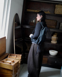 Person standing in a room with wooden furniture and shelves with a black bag on their shoulder.