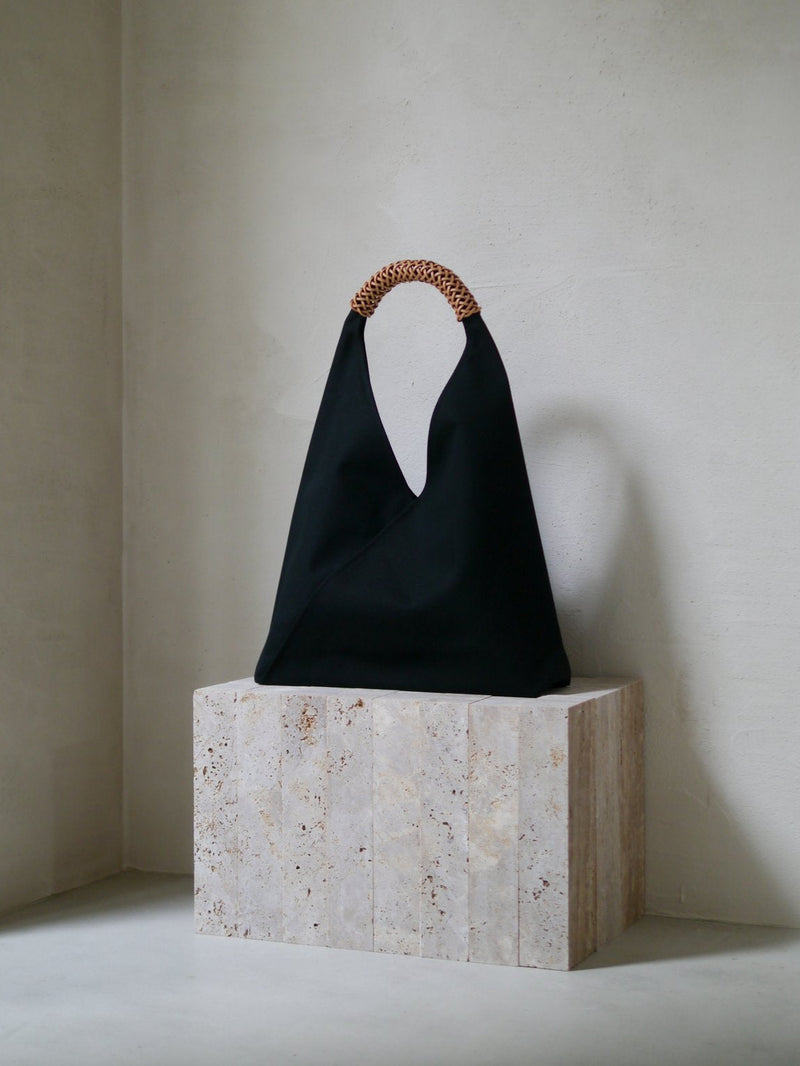 Black bag with a brown leather handle on a stone block against a plain wall
