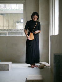 Woman in a black dress wearing a tan bag in a room with windows