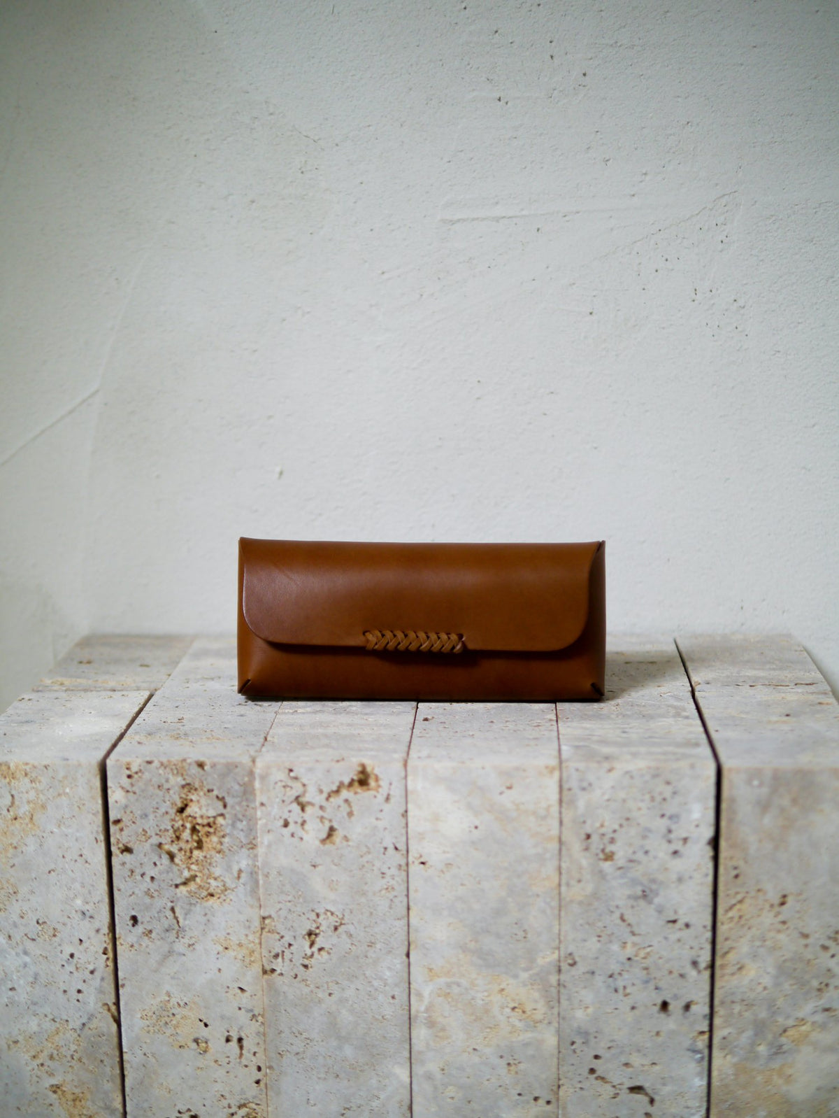 Brown leather glasses case on a textured stone surface with a light gray background