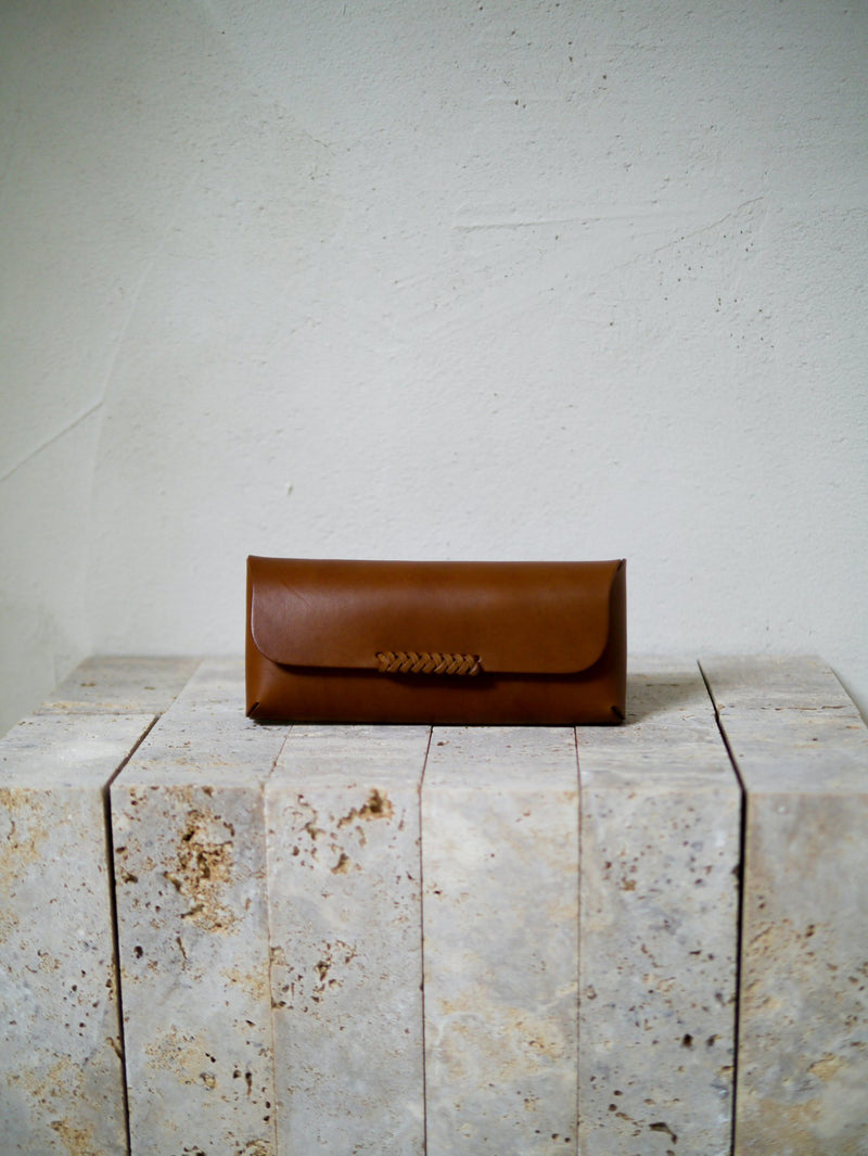 Brown leather glasses case on a textured stone surface with a light gray background