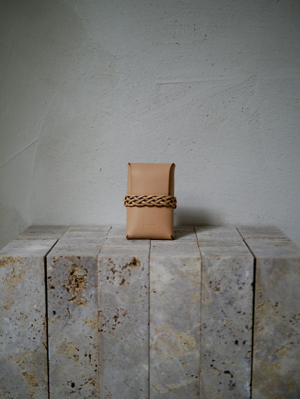 Tan leather pouch with braided handle on a textured stone surface