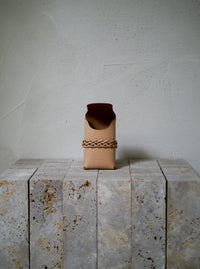 Tan leather pouch with braided design on a textured surface