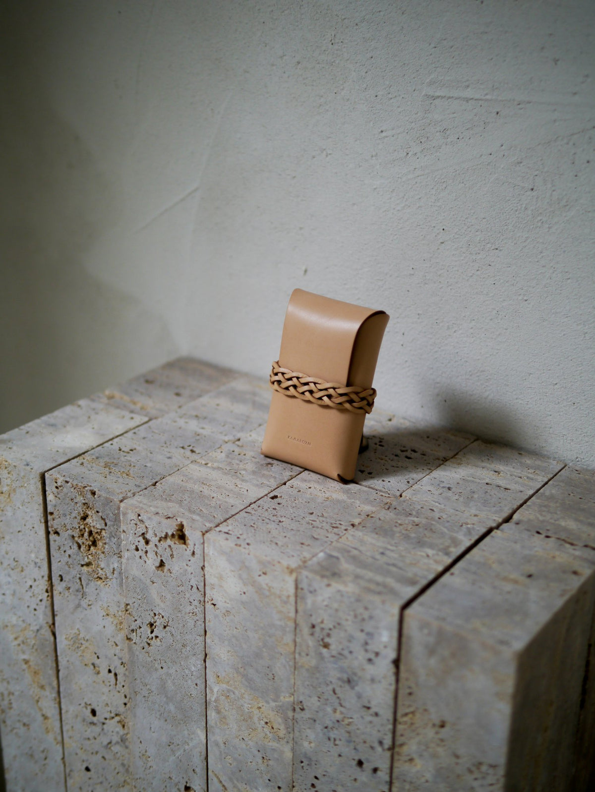 Tan leather pouch with woven detail on a textured stone surface