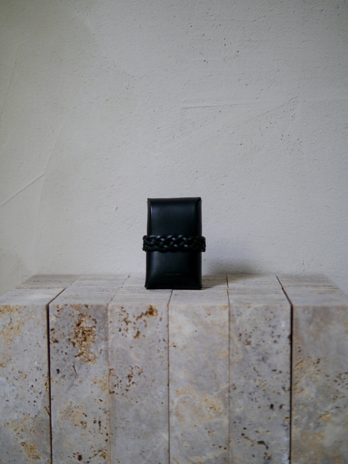 Black leather card case on a textured stone surface with a neutral background
