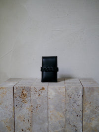 Black leather card case on a textured stone surface with a neutral background