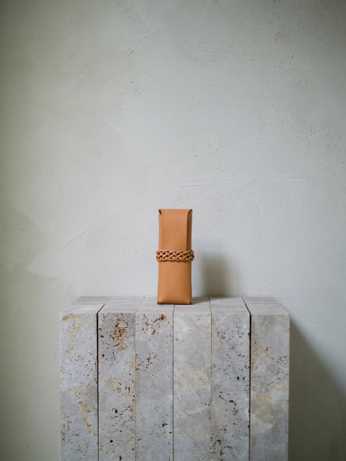 Tan leather case with a woven band on a stone surface against a light background