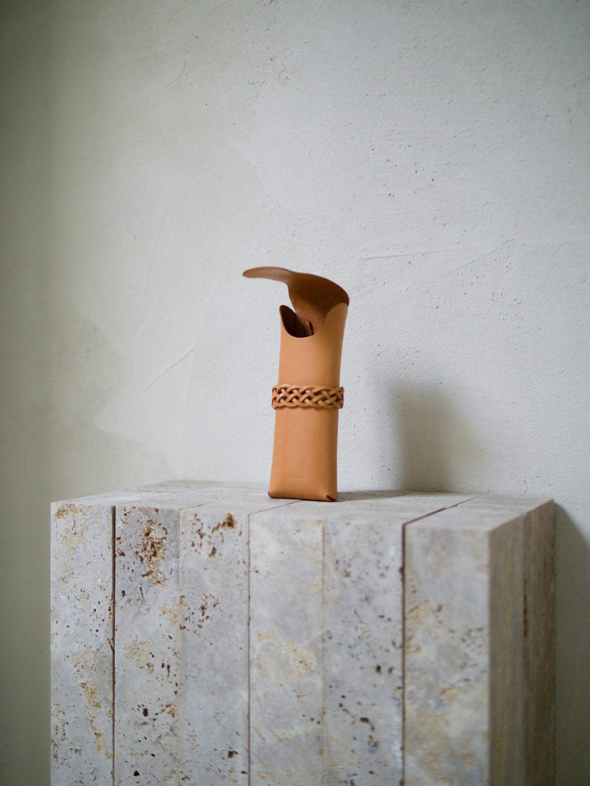 Tan leather case with a woven band on a stone surface against a light background