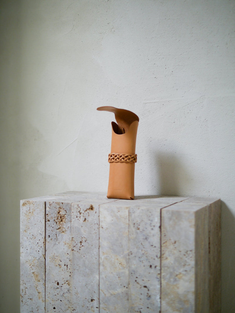 Tan leather case with a woven band on a stone surface against a light background