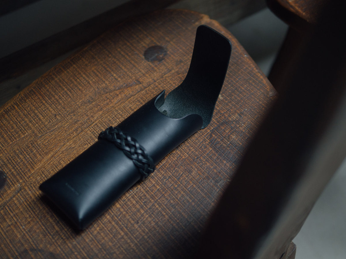 Black leather case with braided strap on a wooden surface