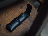 Black leather case with braided strap on a wooden surface