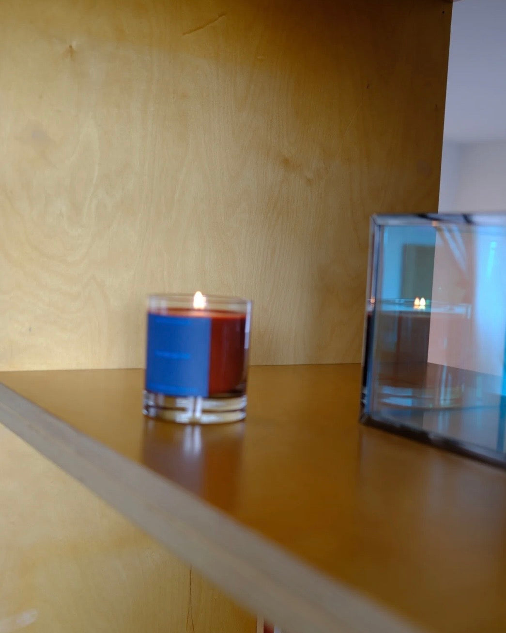 Lit candle on a wood shelf with a blue label