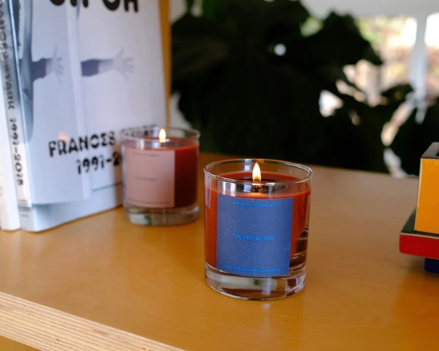 Lit candle in a glass jar with a blue label on a bookshelf