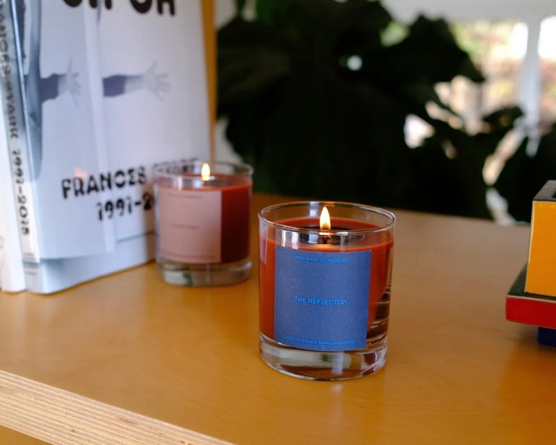 Lit candle in a glass jar with a blue label on a bookshelf