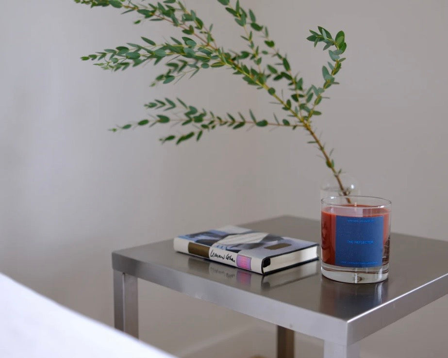 Glass jar candle with a blue label on a side table with a book and plant