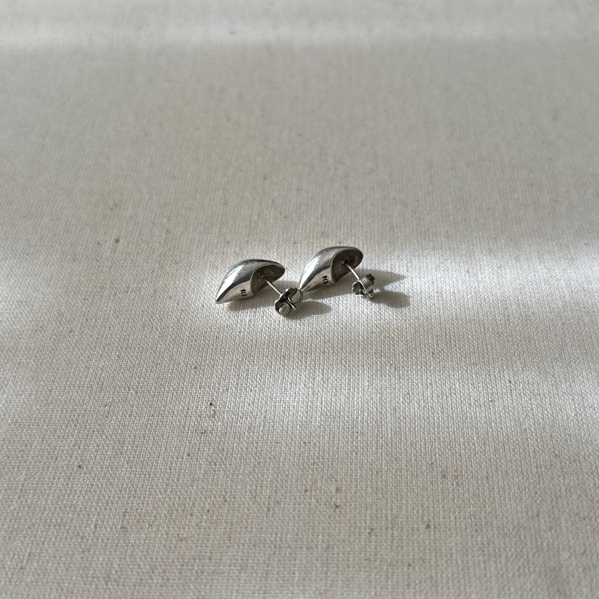 Pair of silver earrings on a light gray fabric background