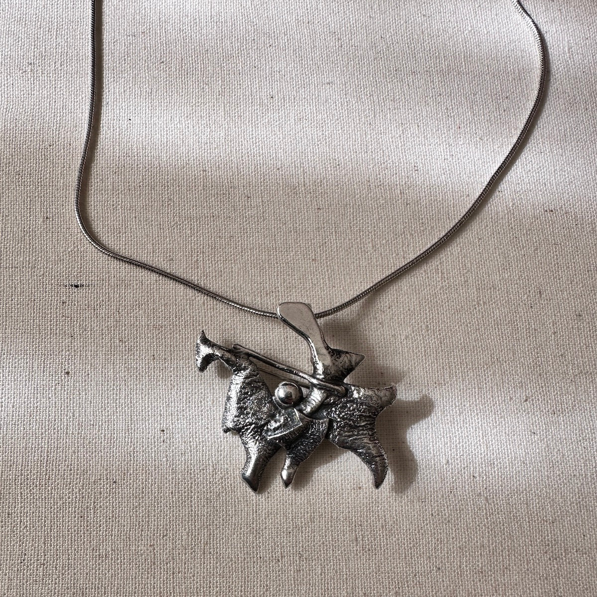 Silver pendant on a chain against a light background