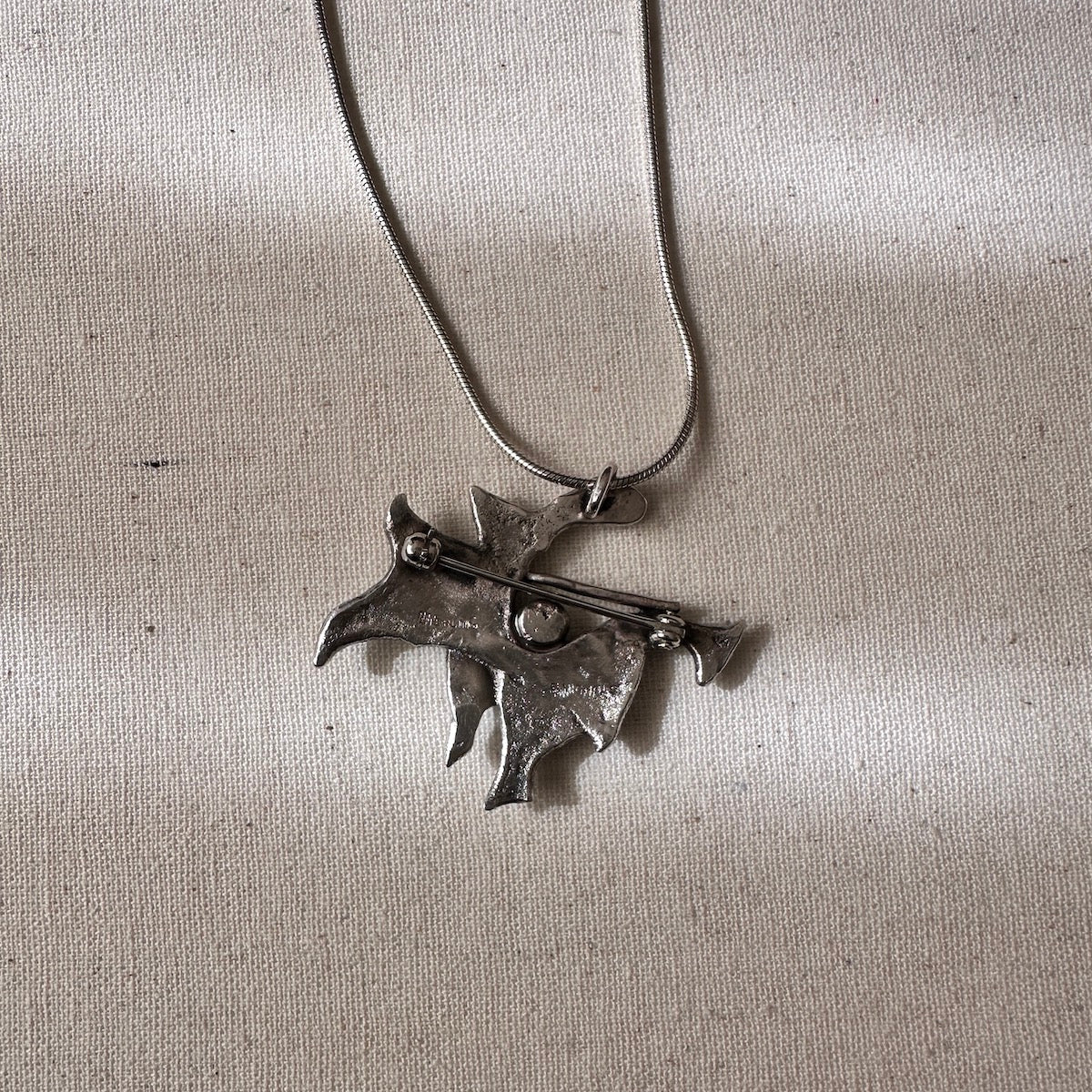 Silver necklace with a unique pendant on a light textured fabric background