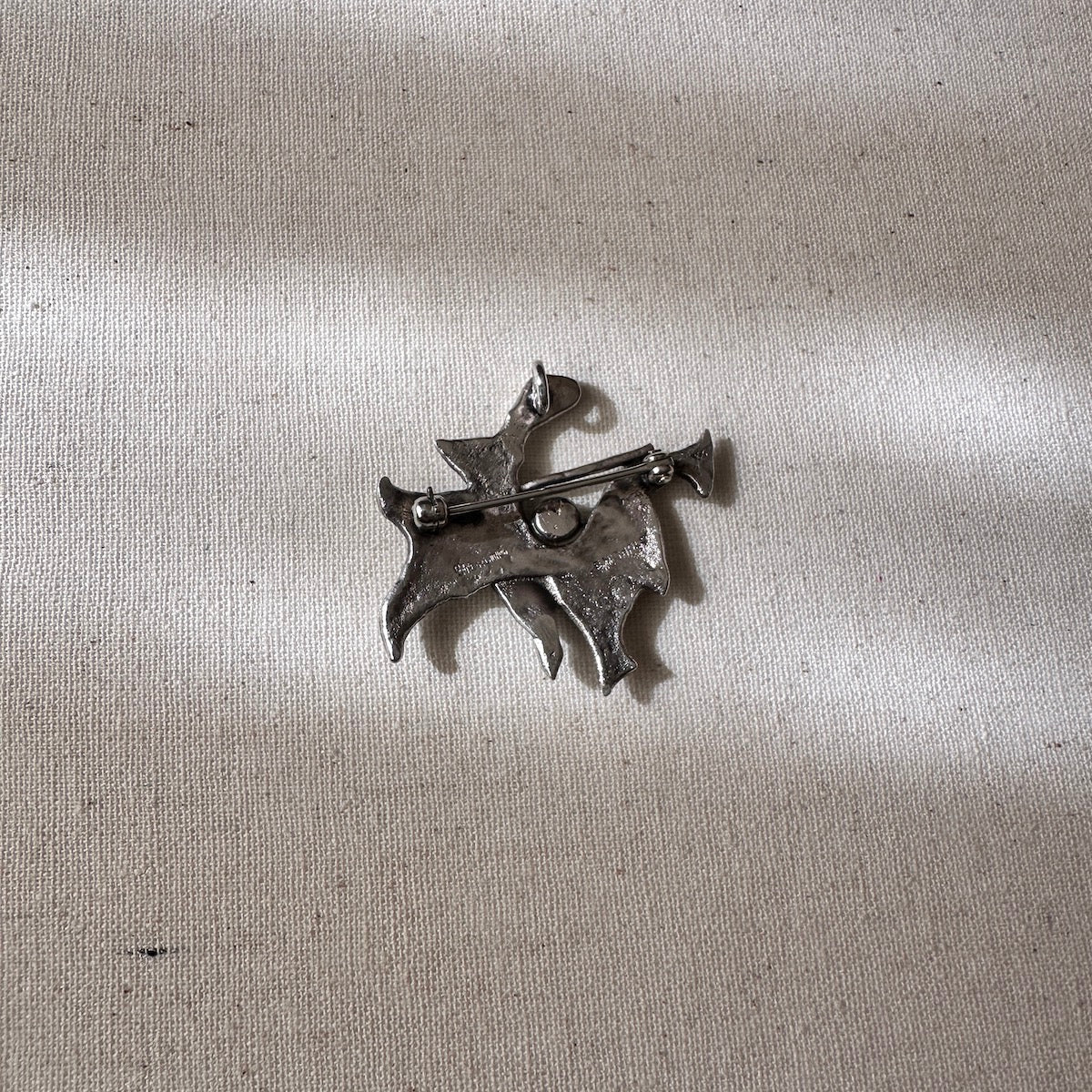 Back of a Silver brooch on a textured beige fabric background