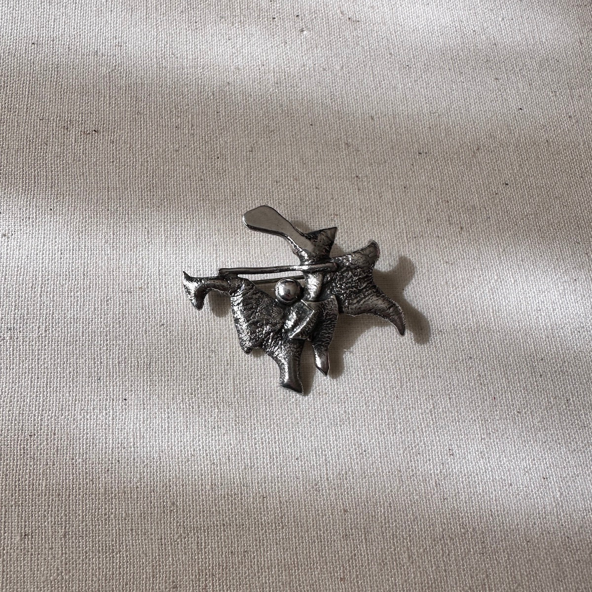 Metallic silver brooch/pendant on a textured fabric background