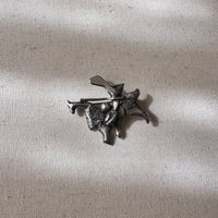 Metallic silver brooch/pendant on a textured fabric background