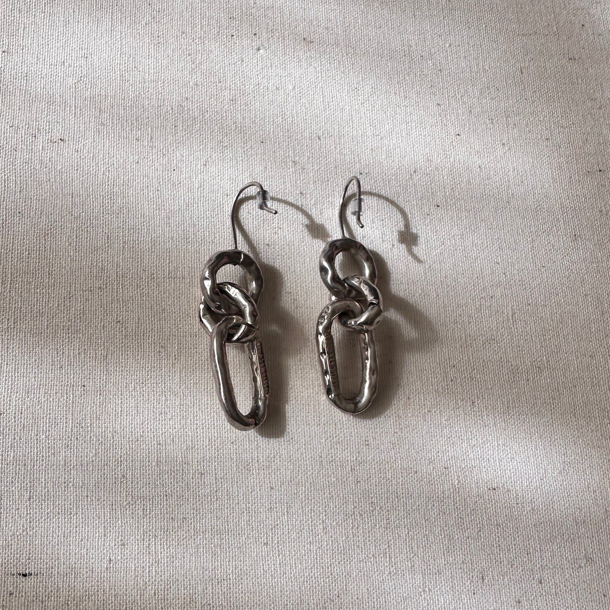 Pair of silver chain-link earrings on a textured beige surface