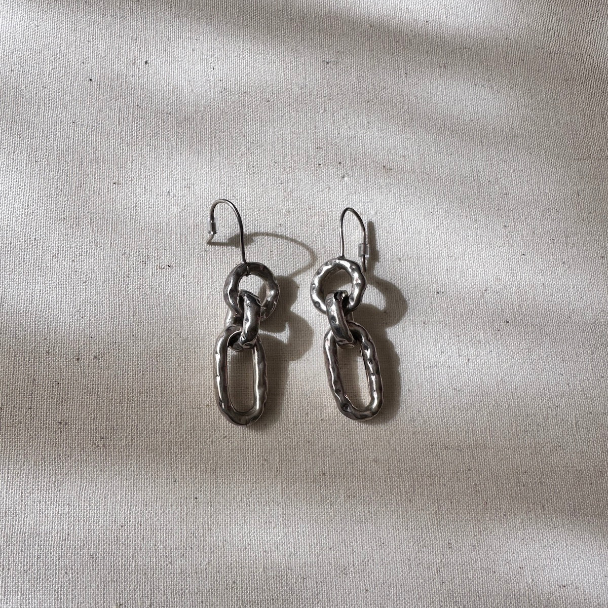 Pair of silver chain link earrings on a textured beige surface