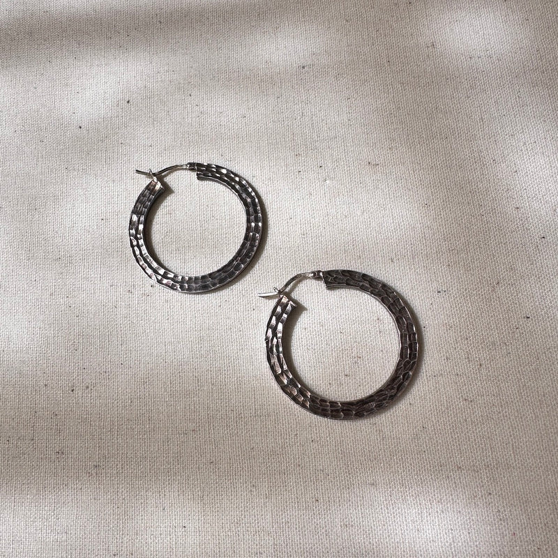 Pair of silver hoop earrings on a textured beige surface