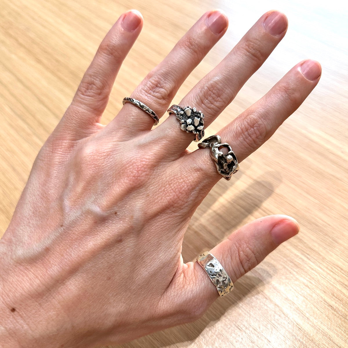 Hand wearing multiple silver rings on a wooden background