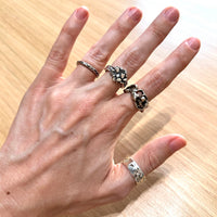 Hand wearing multiple silver rings on a wooden background