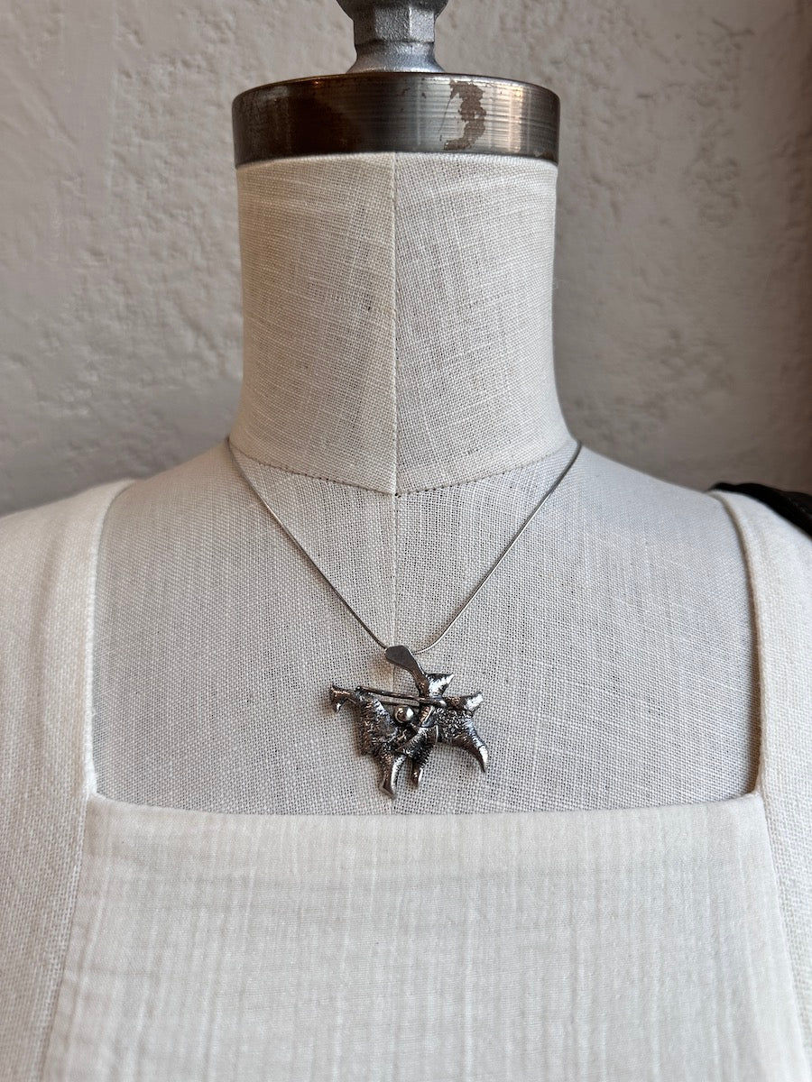 Silver necklace with a detailed pendant on a mannequin against a neutral background