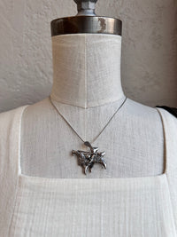 Silver necklace with a detailed pendant on a mannequin against a neutral background