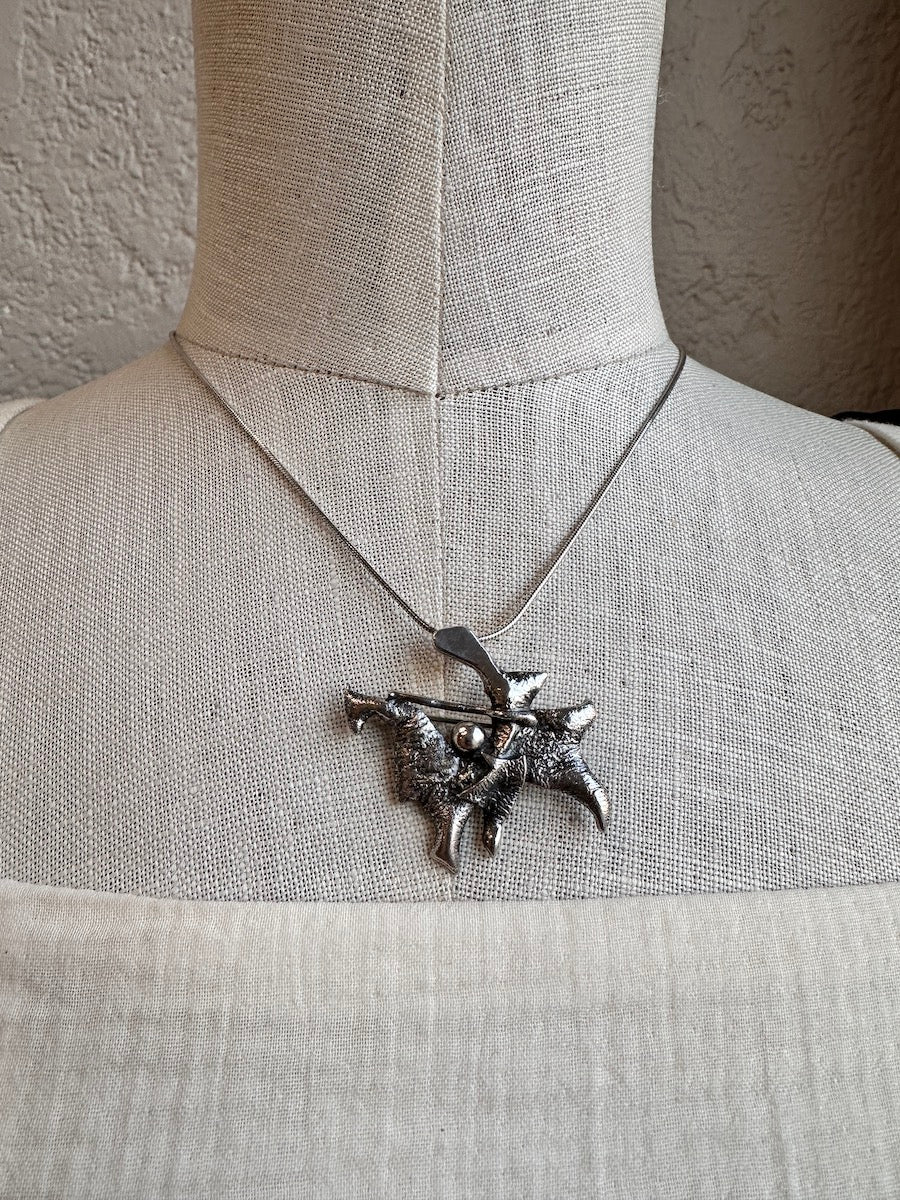 Silver necklace with a detailed pendant on a mannequin against a neutral background