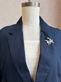 Navy blazer on a mannequin with a decorative silver brooch against a neutral background