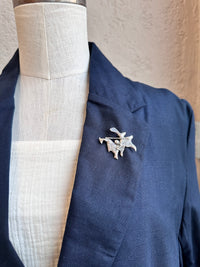 Navy blazer with a decorative brooch on a mannequin against a neutral background