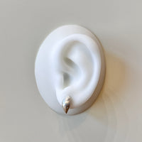 White silicone ear with a silver earring on a light gray background