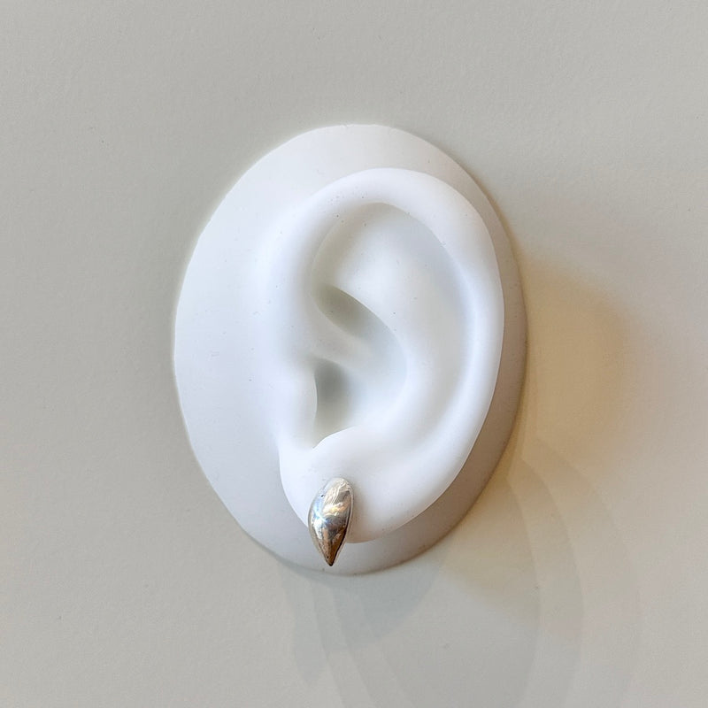 White silicone ear with a silver earring on a light gray background