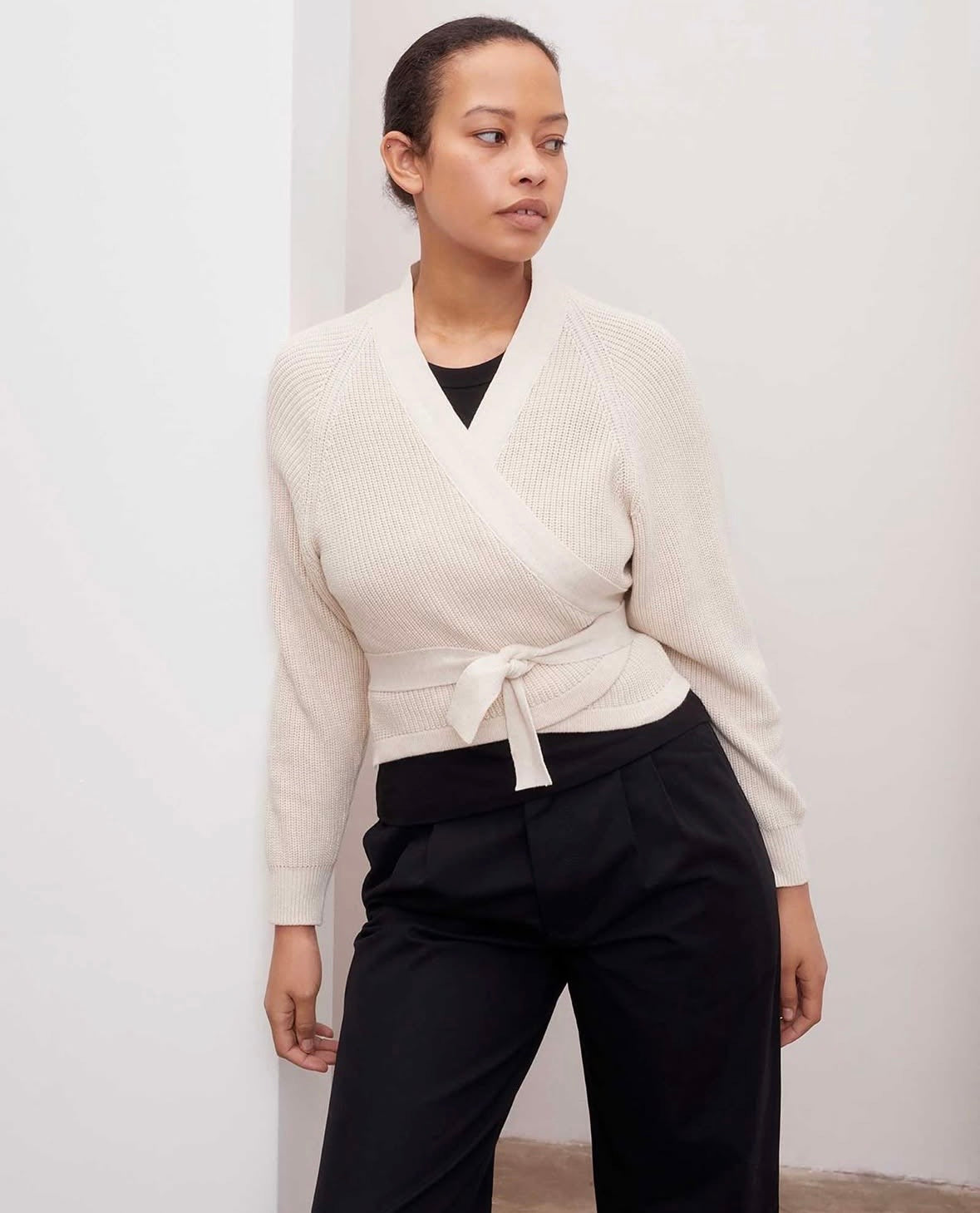 Woman wearing a cream cardigan and black pants against a white background