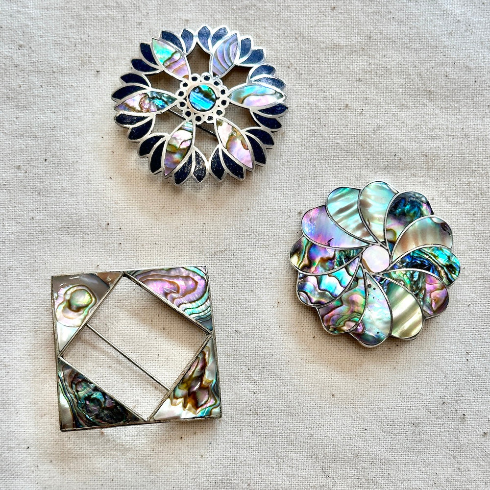 Three decorative abalone shell brooches on a textured beige surface