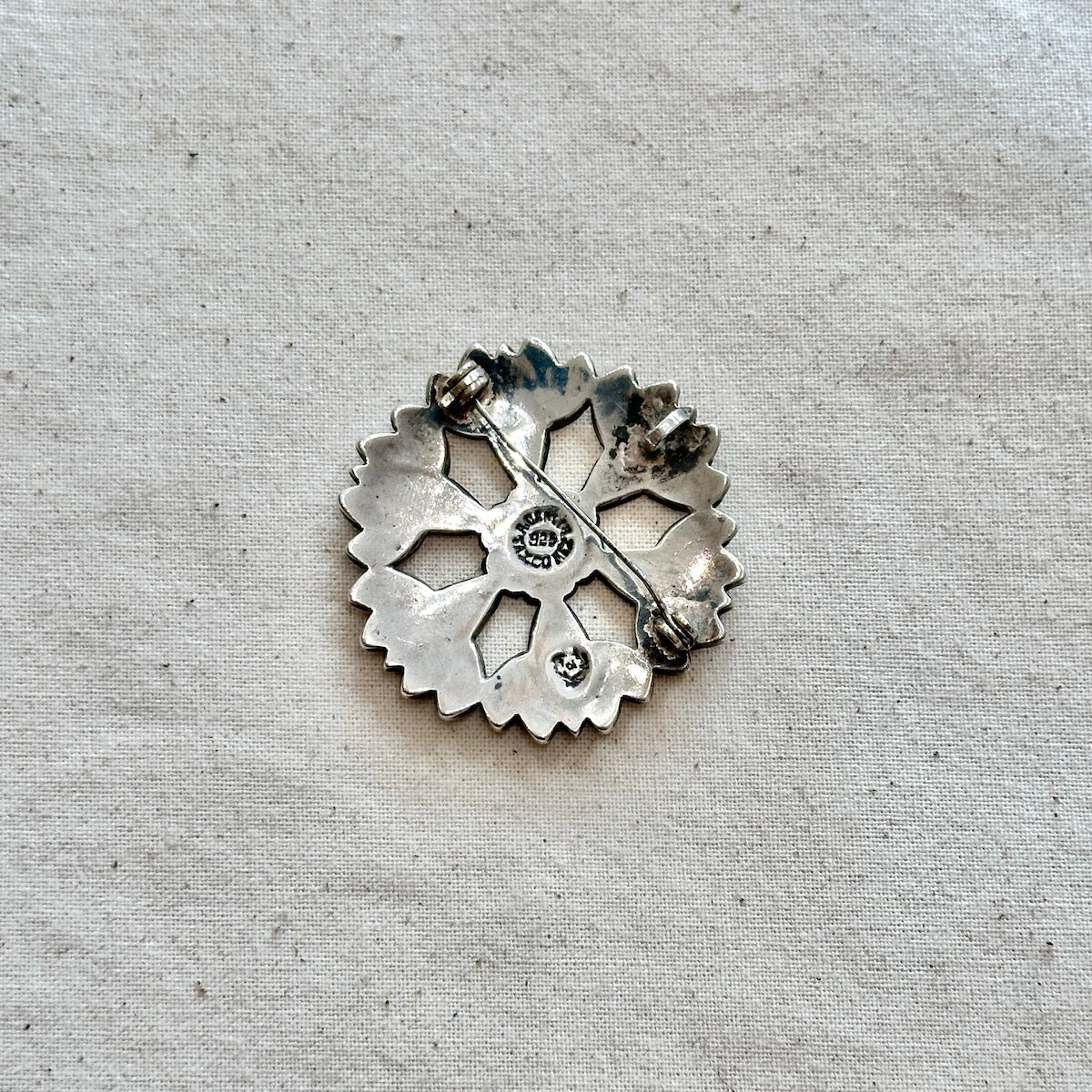 Silver floral-shaped brooch/pendant on a textured gray background