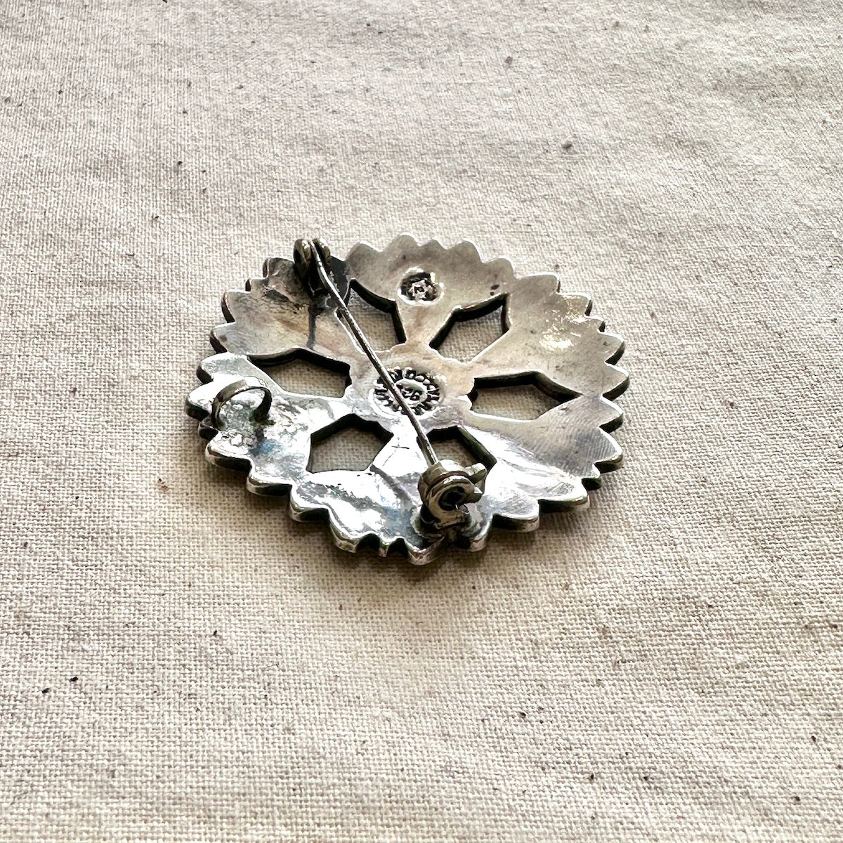 Silver floral-shaped brooch/pendant on a textured beige fabric background