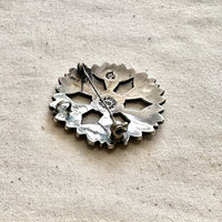 Silver floral-shaped brooch/pendant on a textured beige fabric background
