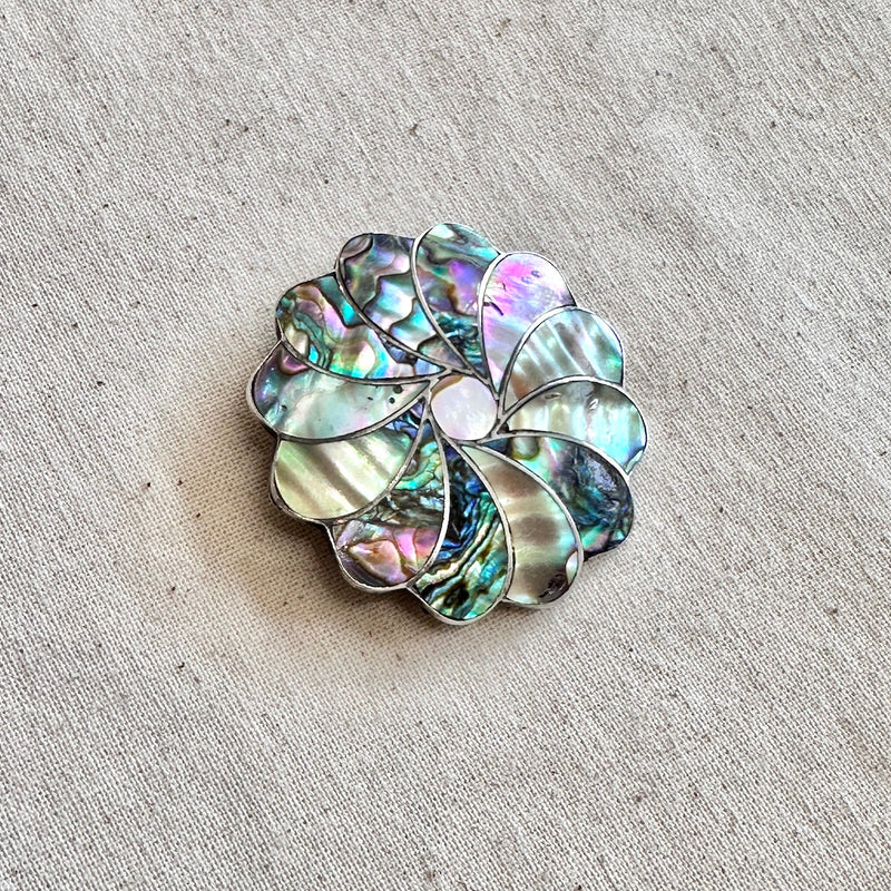 Multicolored abalone shell brooch on a textured beige surface