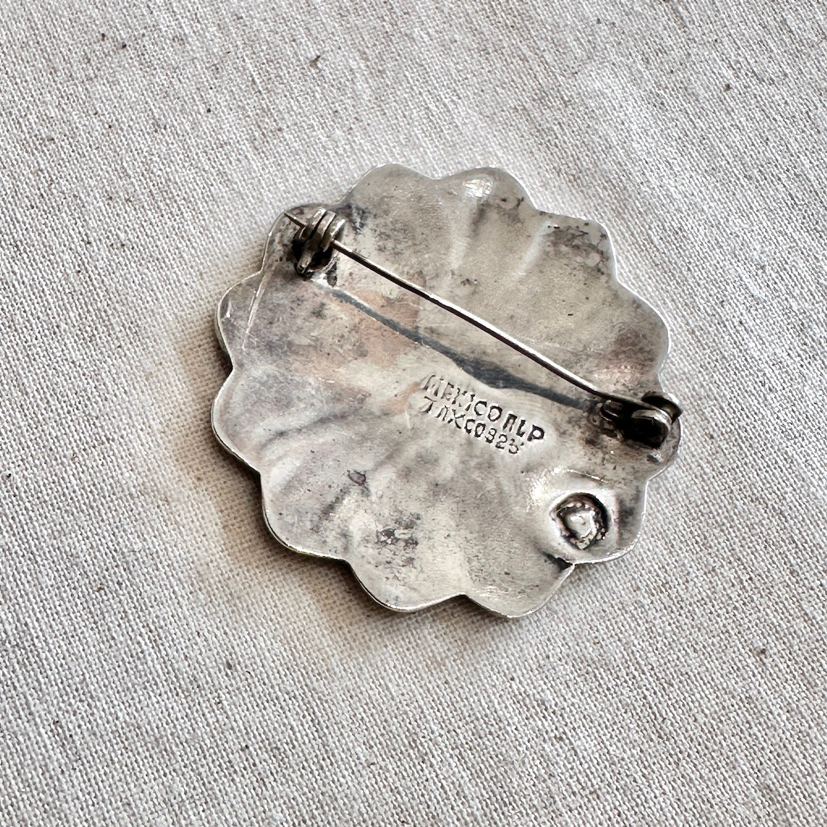 Silver brooch with 'Mexico' inscription on a textured fabric background