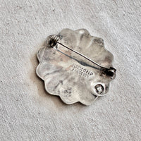 Silver brooch with 'Mexico' inscription on a textured fabric background