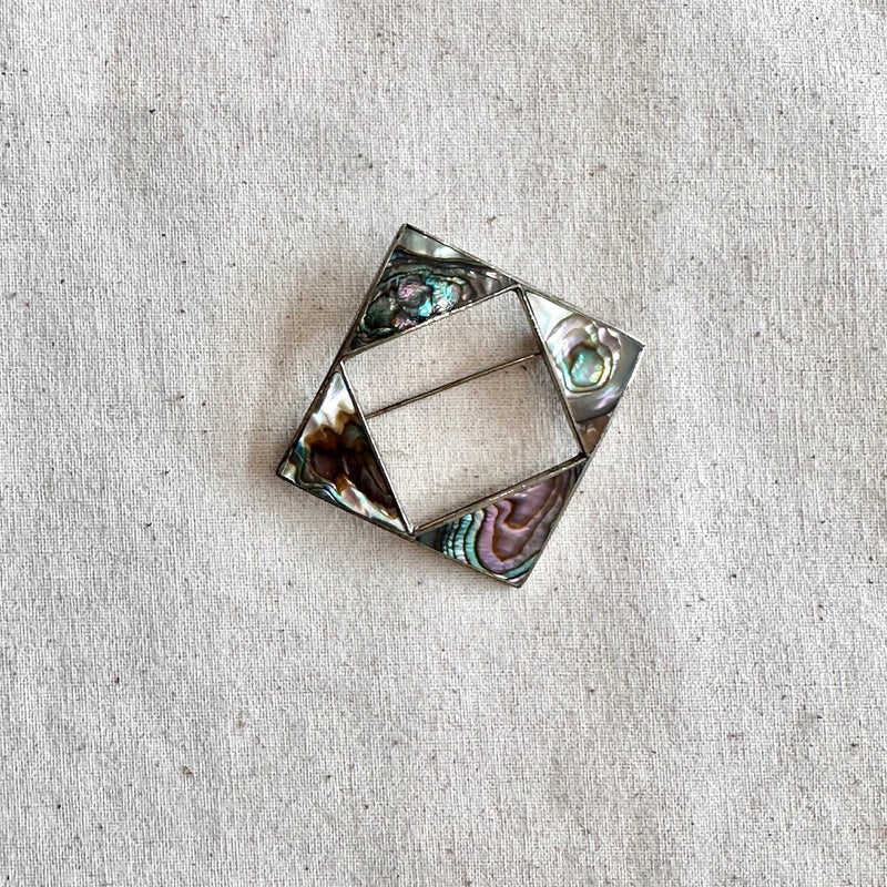 Decorative brooch with abalone shell inlay on a textured beige background