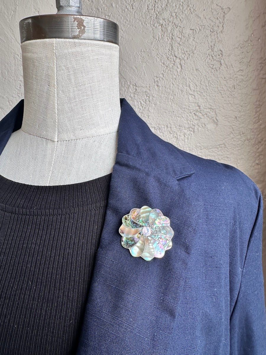 Navy blazer with a decorative brooch on a mannequin against a neutral wall.