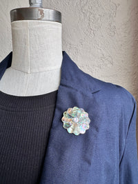 Navy blazer with a decorative brooch on a mannequin against a neutral wall.