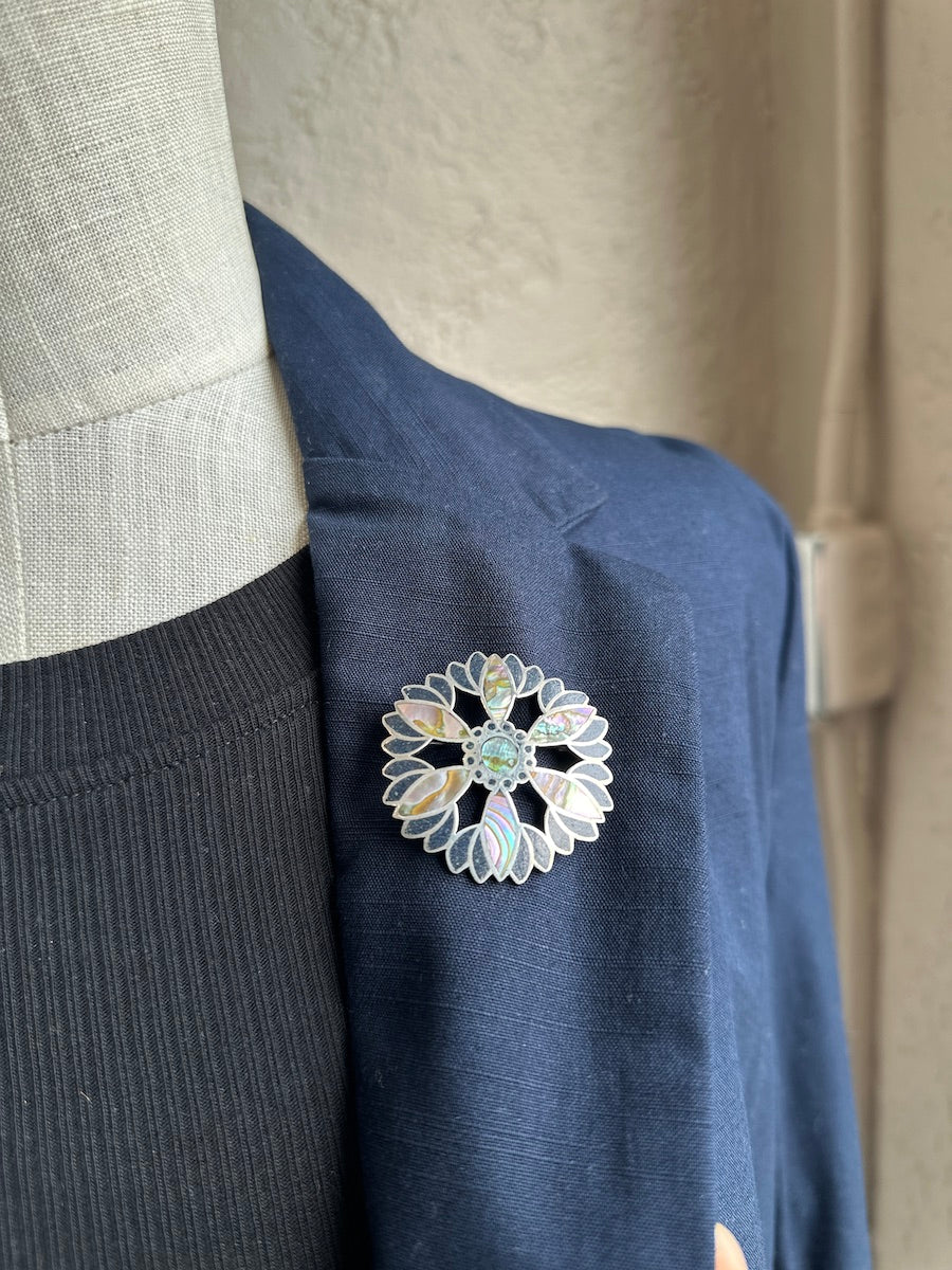 Close-up of a decorative brooch on a navy blue garment with a neutral background